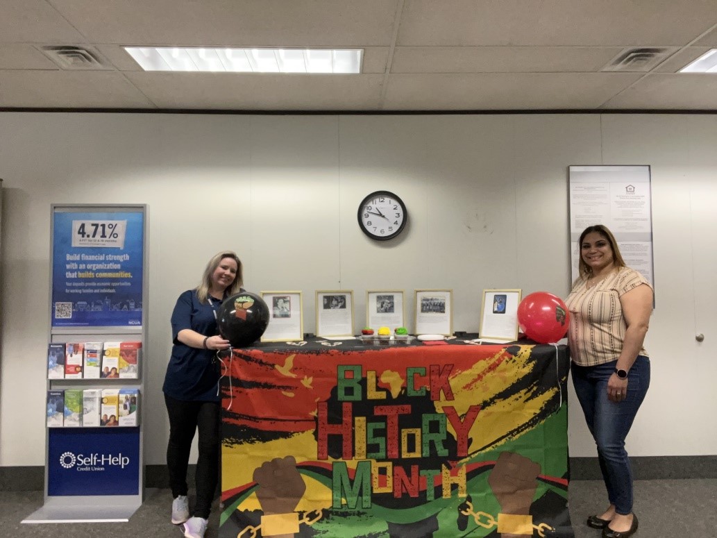 two smiling women standing on either side of a table decorated for Black History Month