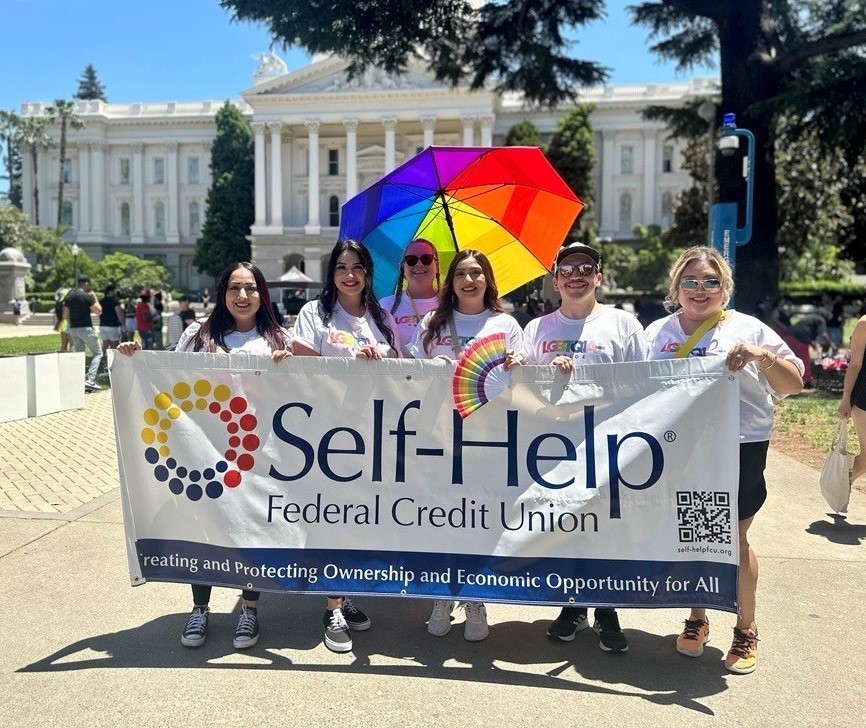 happy people holding a Self-Help Federal Credit Union banner in front of the California Capitol building