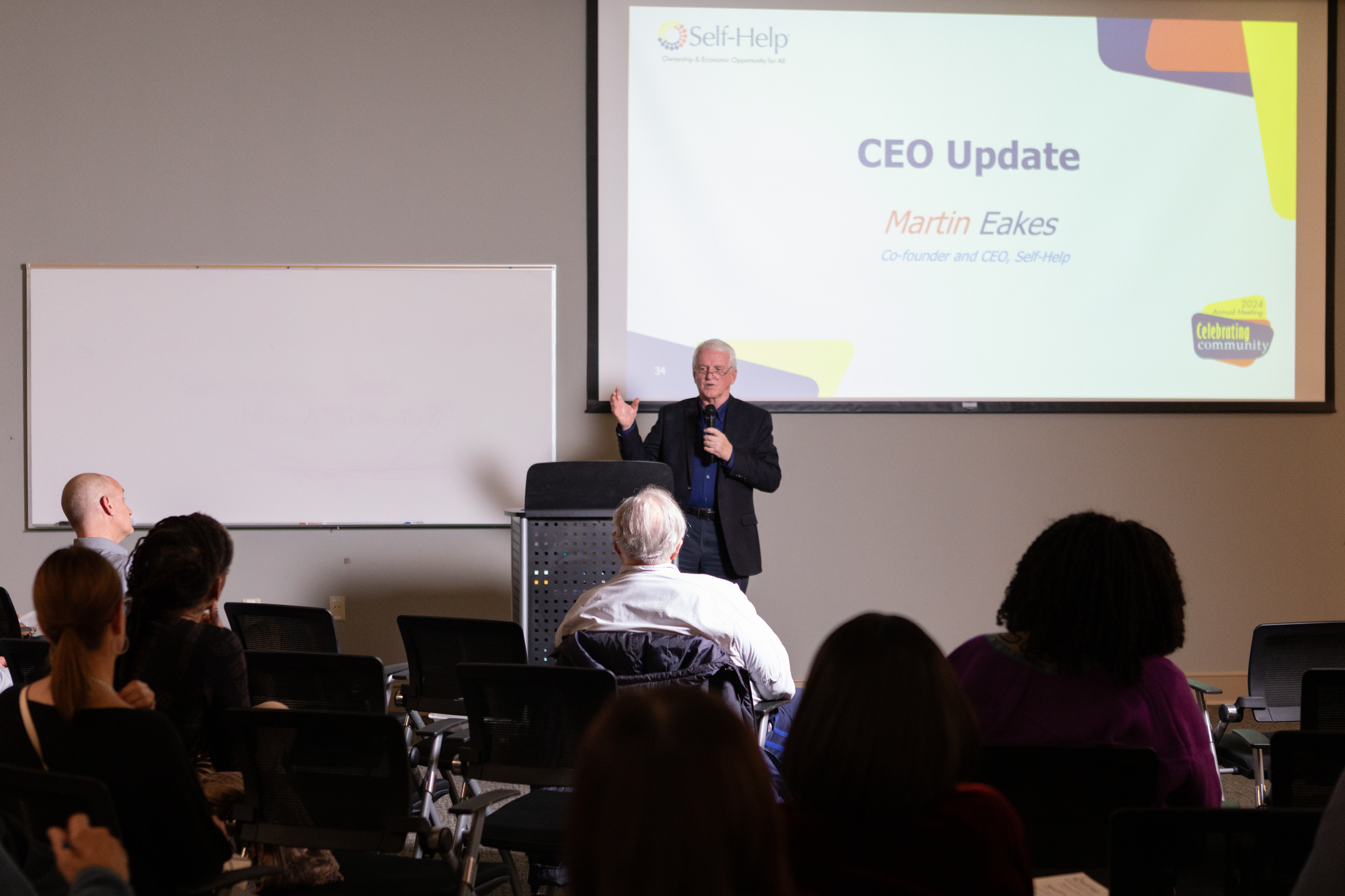 a photo of Self-Help Credit Union's CEO, Martin Eakes, talking into a microphone behind a podium on a stage at Self-Help Credit Union's Annual Members' Meeting in Durham, North Carolina.