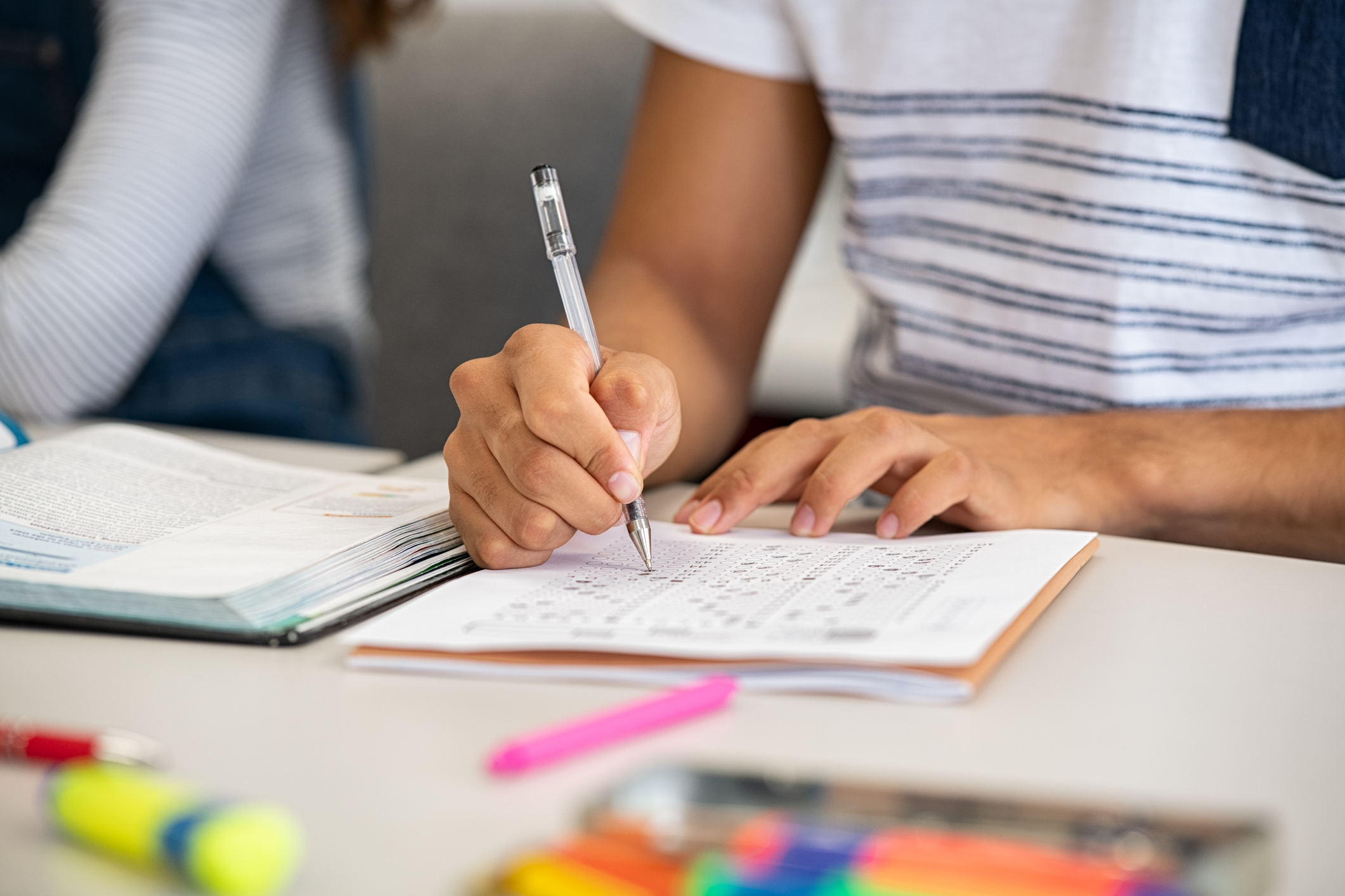 student filling out a scantron with a pen on a table