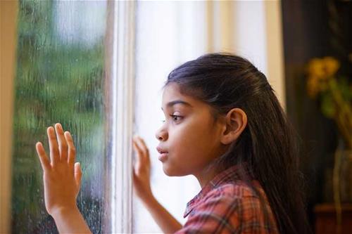 Girl stares at rain through a window